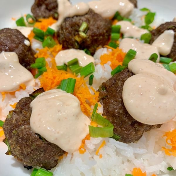 close up image of meatballs topped with firecracker sauce on top of rice with green onions and shredded carrots - part of easy dinners for busy moms article