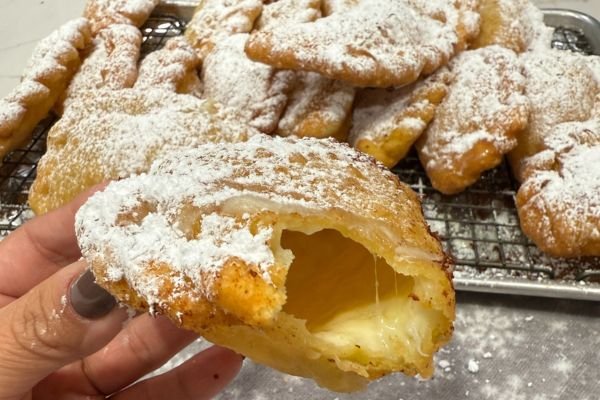A delicious fried pasteles de queso covered in powdered sugar and ripped open to show the melted cheese inside