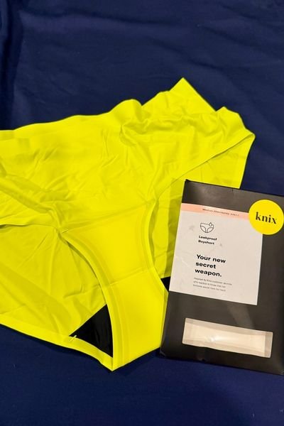flatlay image of the Knix boyshorts in their neon yellow color against a dark blue bed sheet