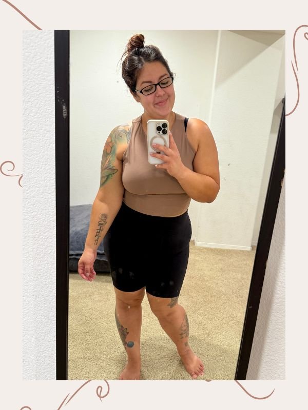 mirror selfie of woman with her hair in a bun, a cropped tan top and black biker shorts