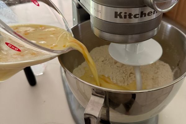 image of liquid ingredients being poured into a kitchenaid mixer full of dry ingredients