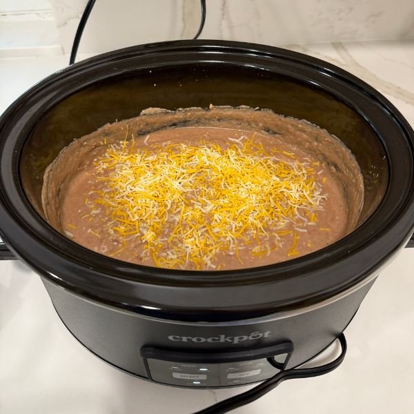 close up image of refried beans with melted cheddar cheese in a crock pot - part of easy dinners for busy moms article